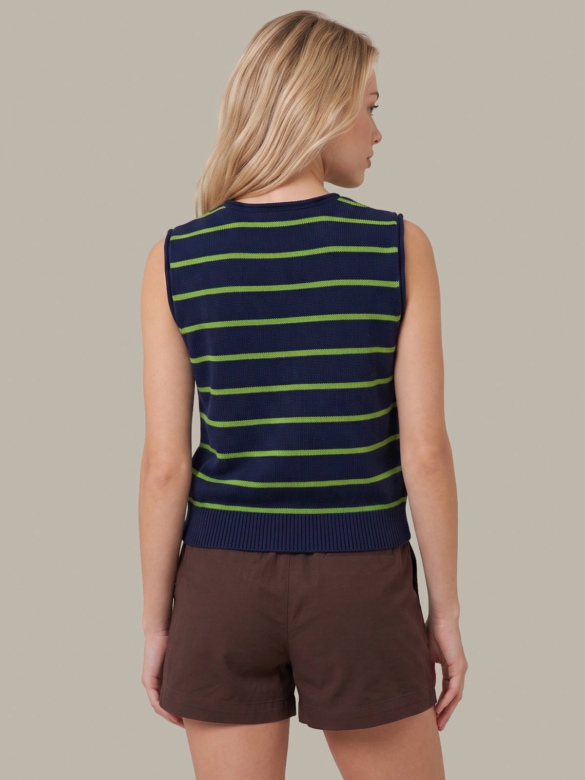 A woman shown from the back wearing a sleeveless knit top with horizontal navy and lime green stripes, paired with brown shorts, against a solid taupe background.