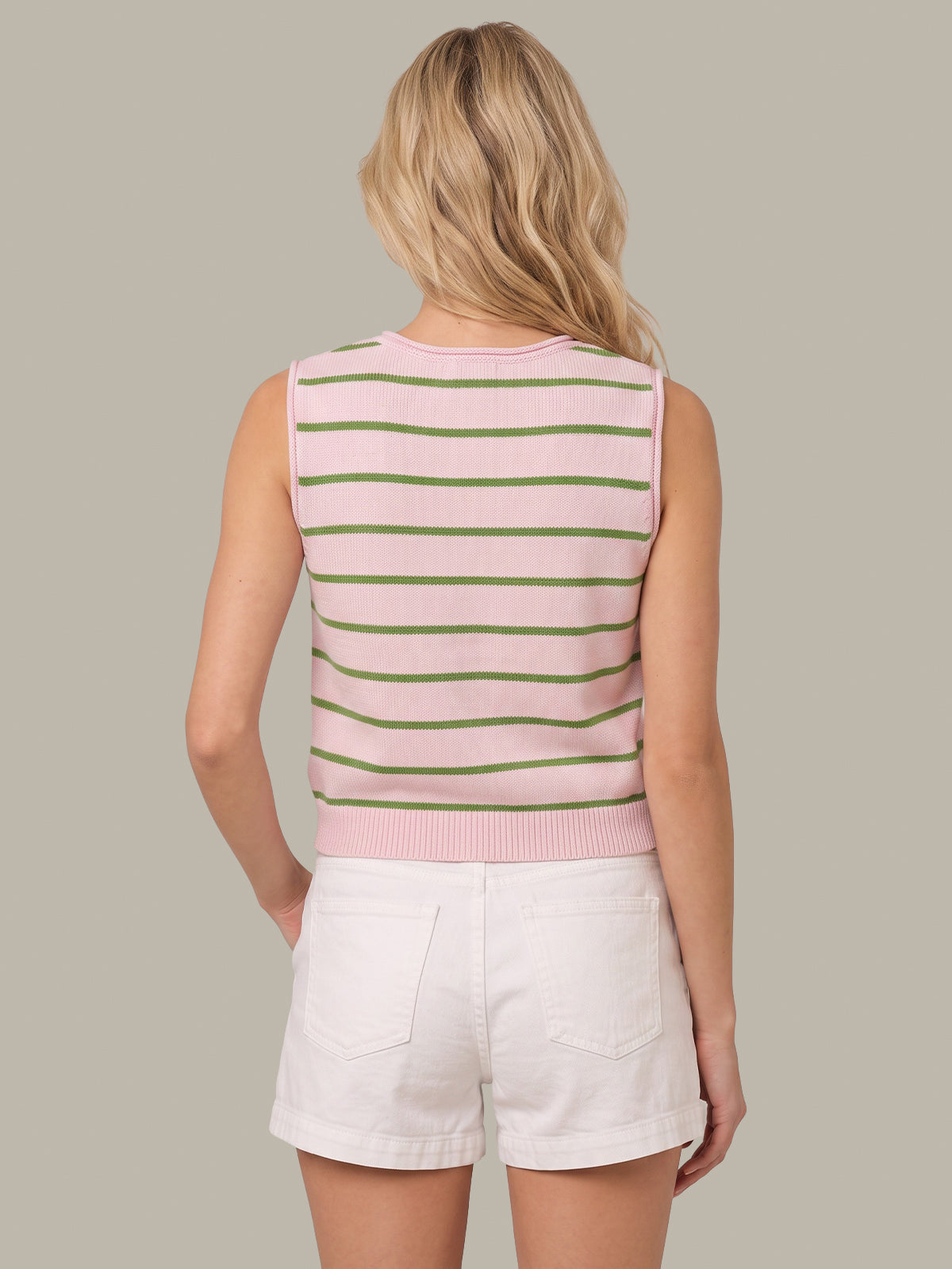 A woman shown from the back wearing a sleeveless knit top with horizontal pink and olive green stripes, paired with white shorts, against a solid taupe background.