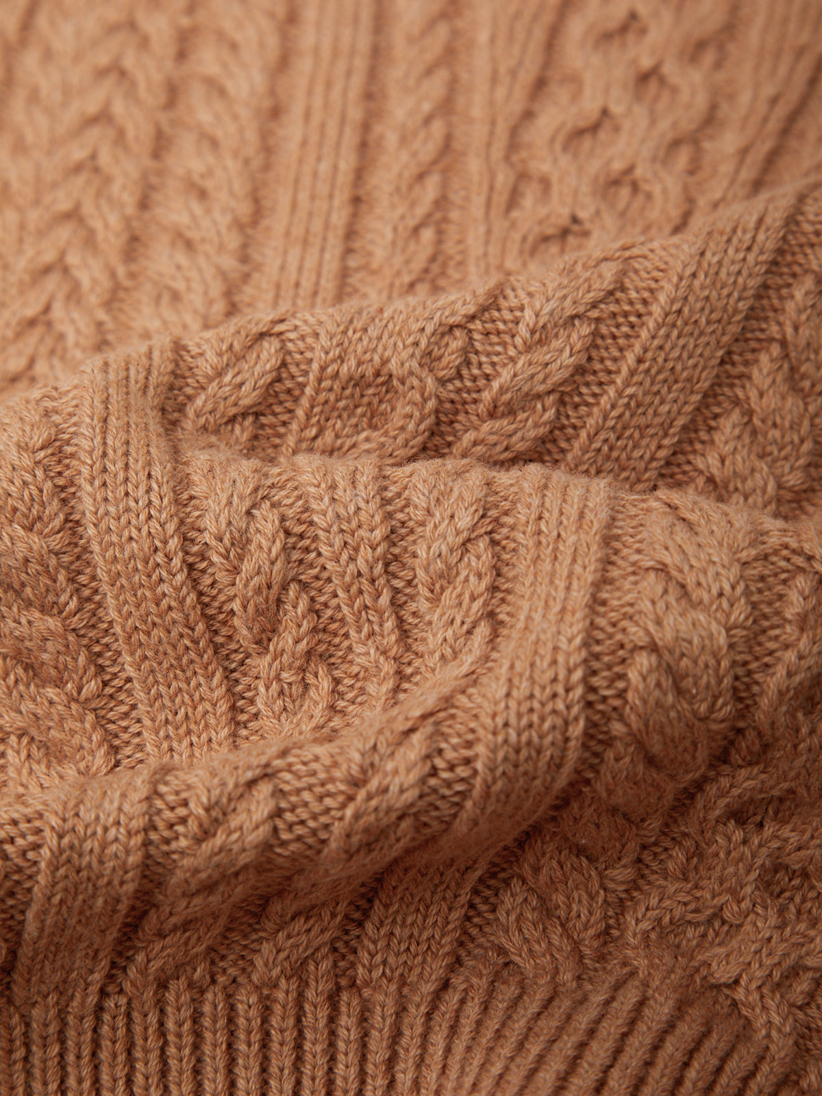 Close-up of a warm camel-colored cable-knit sweater showing detailed knit patterns and soft folds.