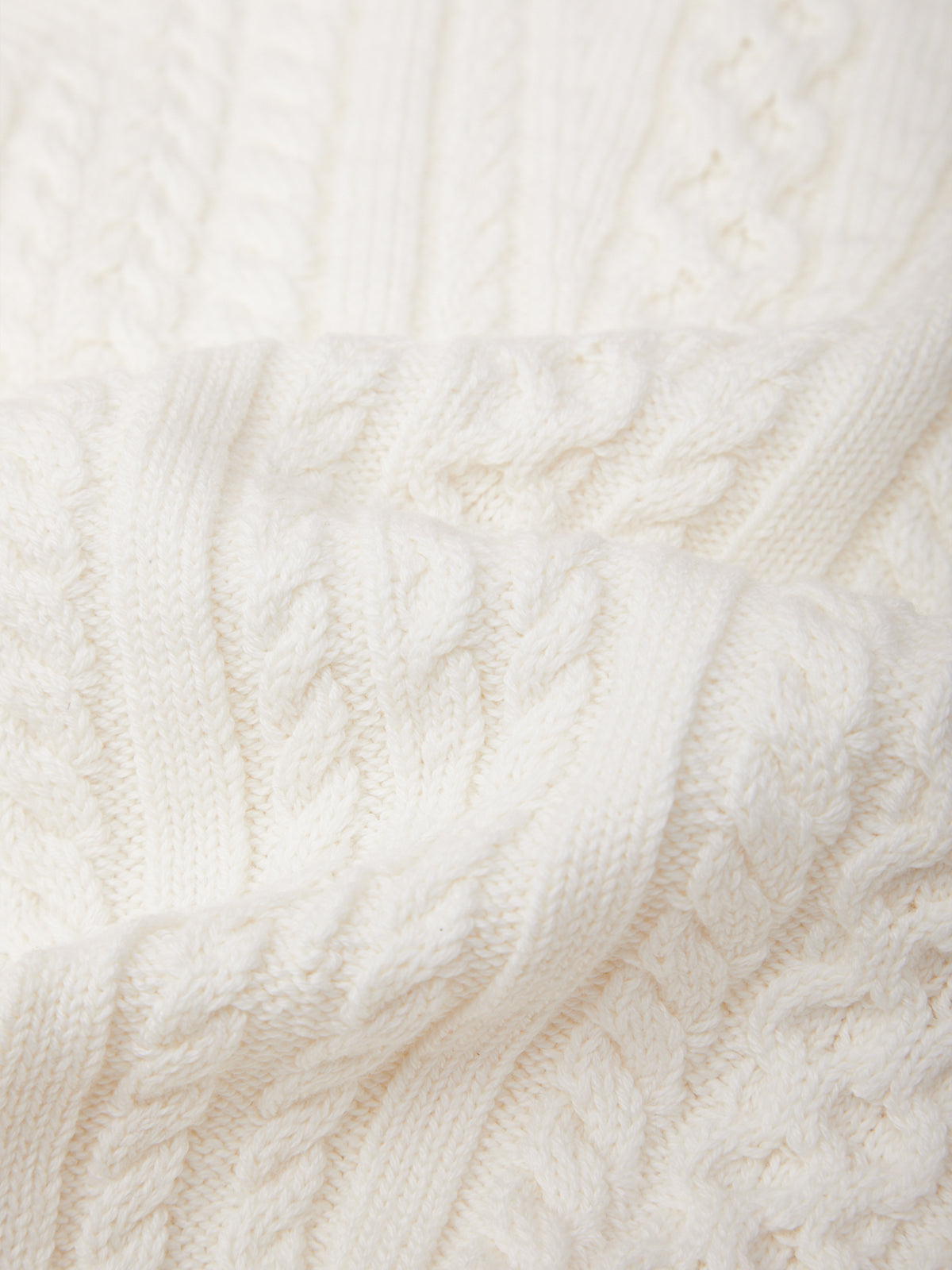 Close-up of a cream-colored cable-knit fabric with detailed knit patterns and soft folds.