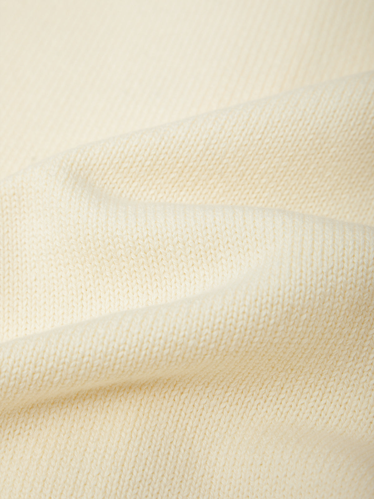 A close-up of a cream-colored knit fabric with soft folds showing the fine texture of the material.