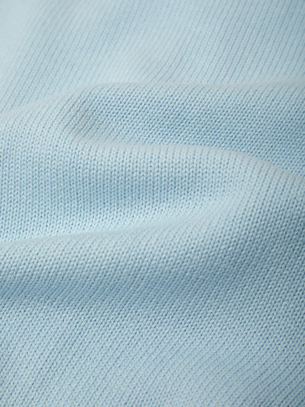 A close-up of light blue knit fabric with a fine ribbed texture and soft folds.