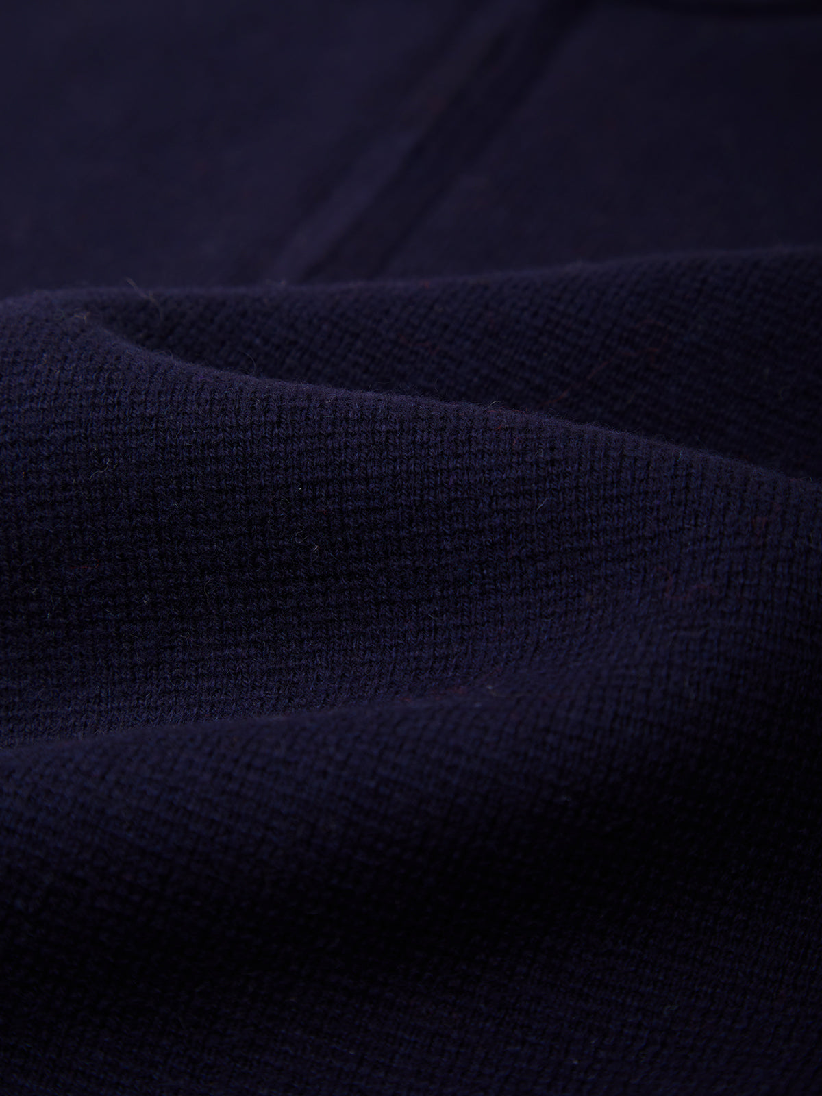 Close-up of dark navy blue ribbed knit fabric with soft folds and a textured waffle-like surface.