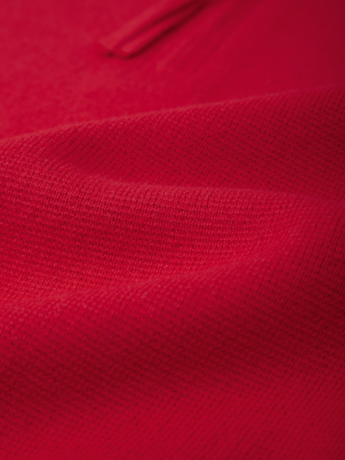 A close-up of bright red knit fabric with soft folds and a subtle sheen, showing the texture and color of the material.