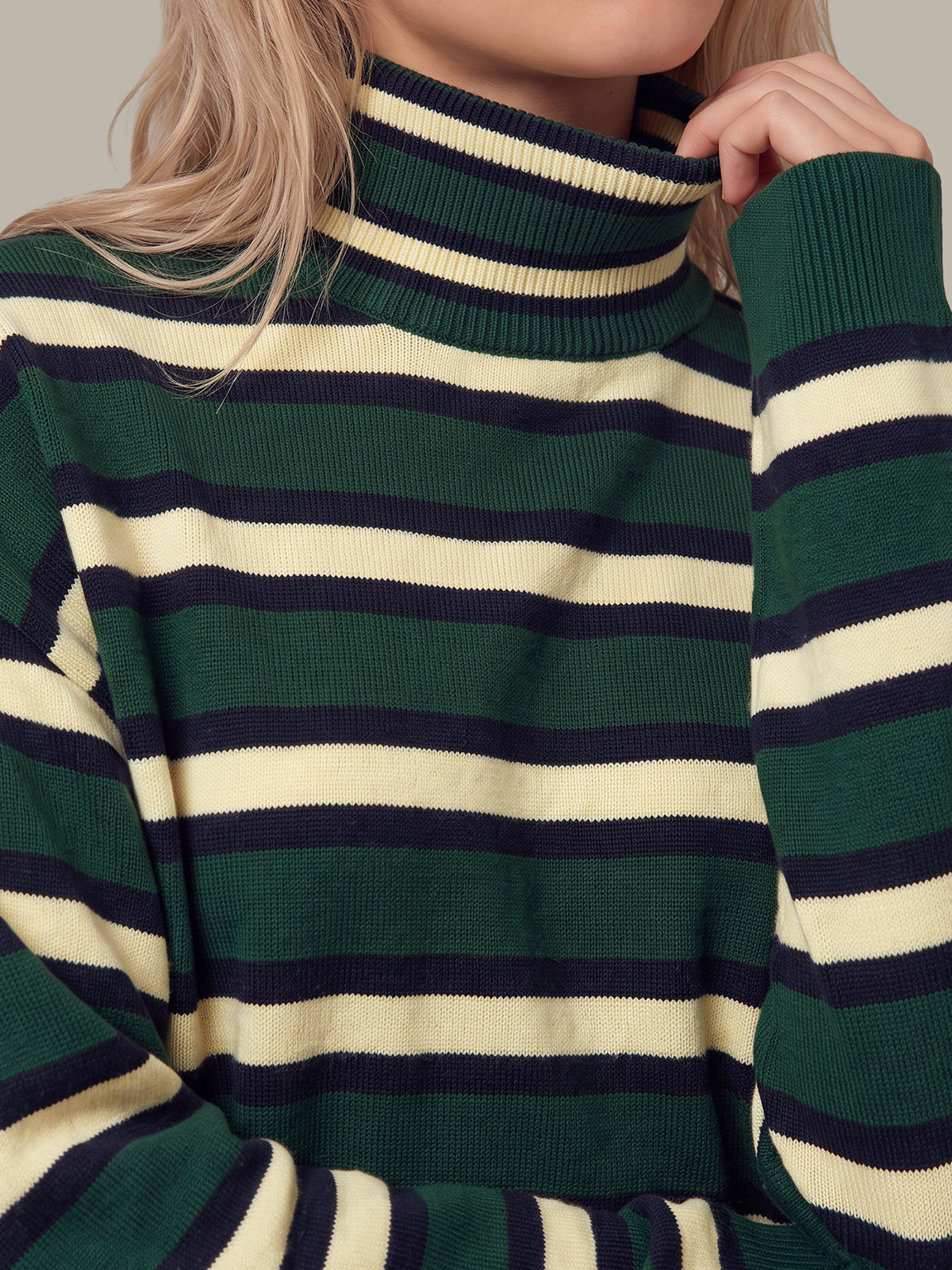A close-up of a woman wearing a ribbed turtleneck sweater with horizontal stripes in forest green, cream, and navy blue.
