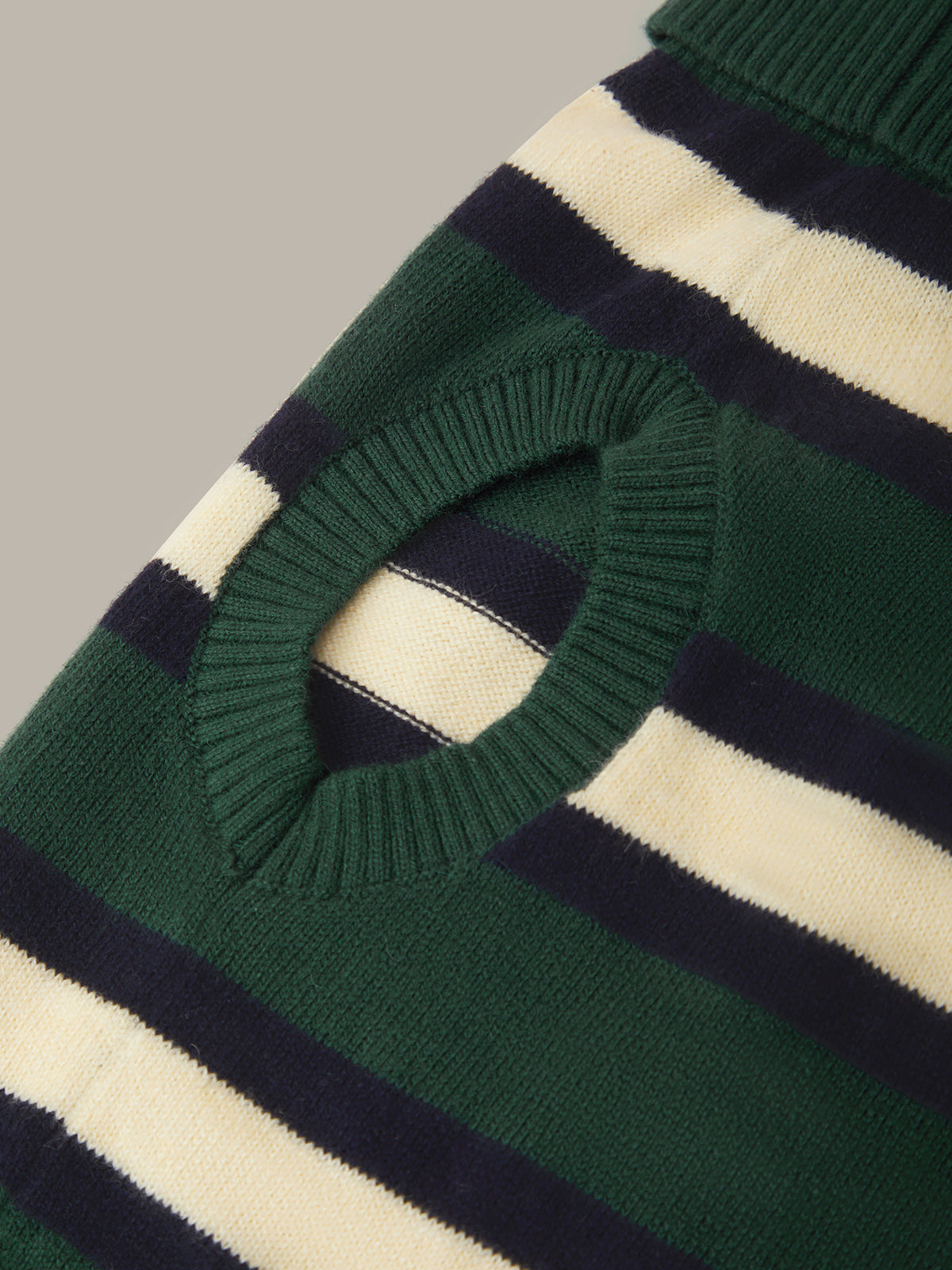 Close-up of a striped knit sweater with a circular cutout, featuring dark green, navy blue, and cream horizontal stripes.