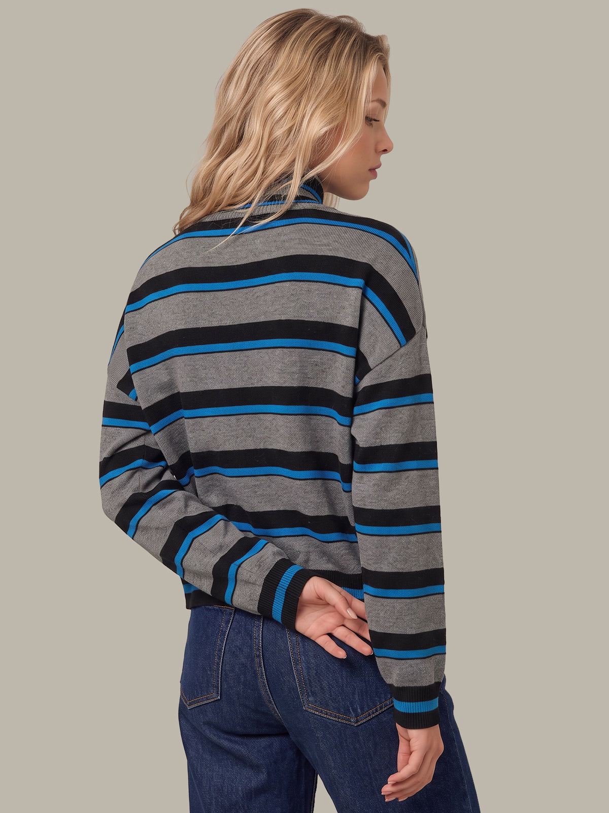 A woman shown from the back wearing a gray long-sleeve striped sweater with black and blue horizontal stripes, paired with dark blue jeans, against a solid light gray background.