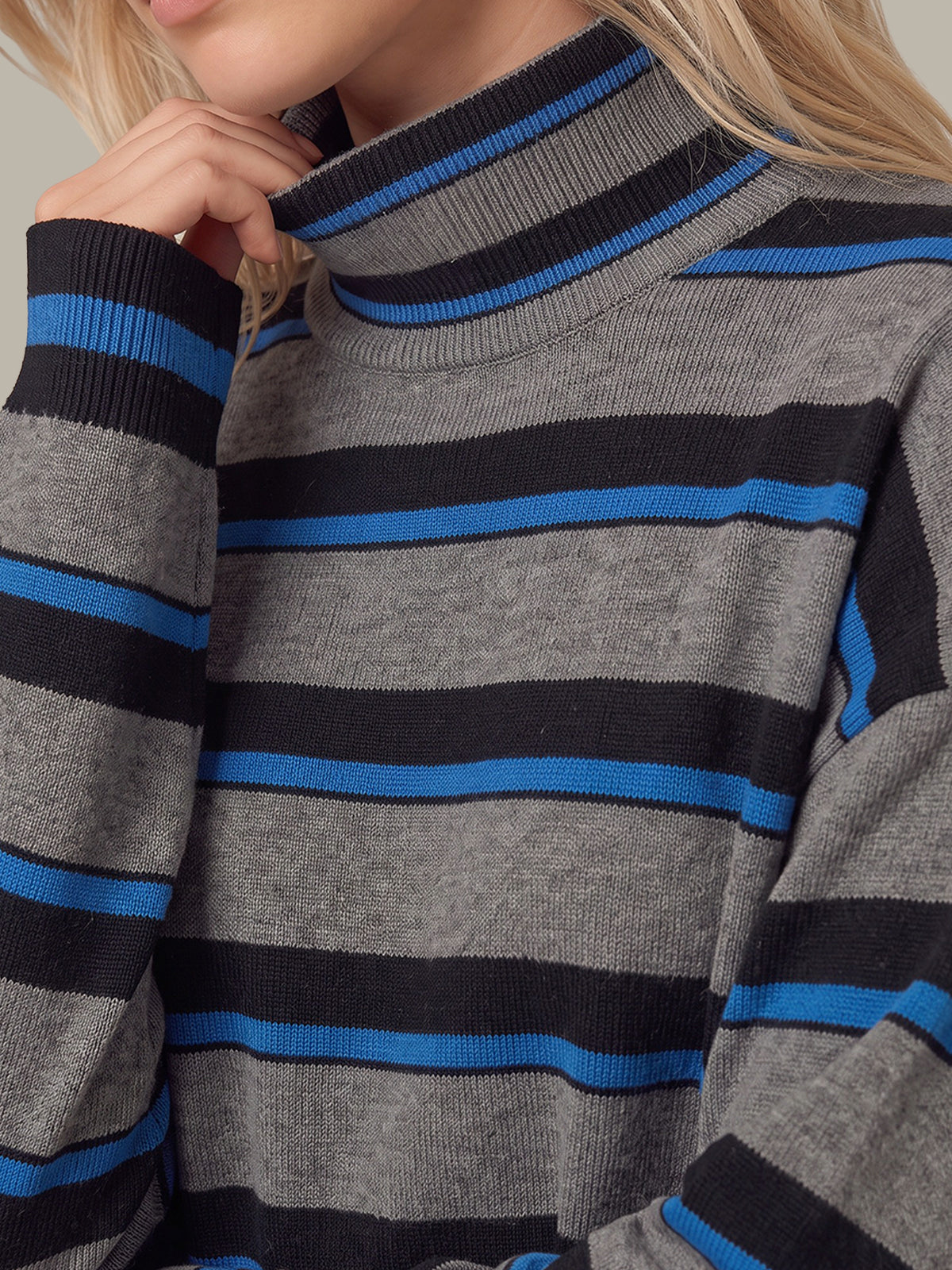 Close-up of a person wearing a gray ribbed turtleneck sweater with horizontal black and bright blue stripes.