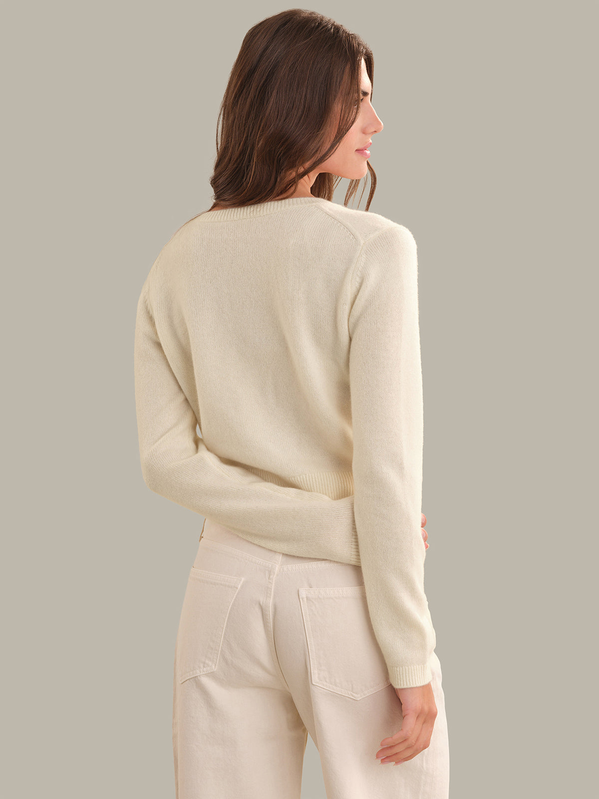 A woman shown from the back wearing a cream-colored knit sweater and matching cream pants against a solid light gray background.