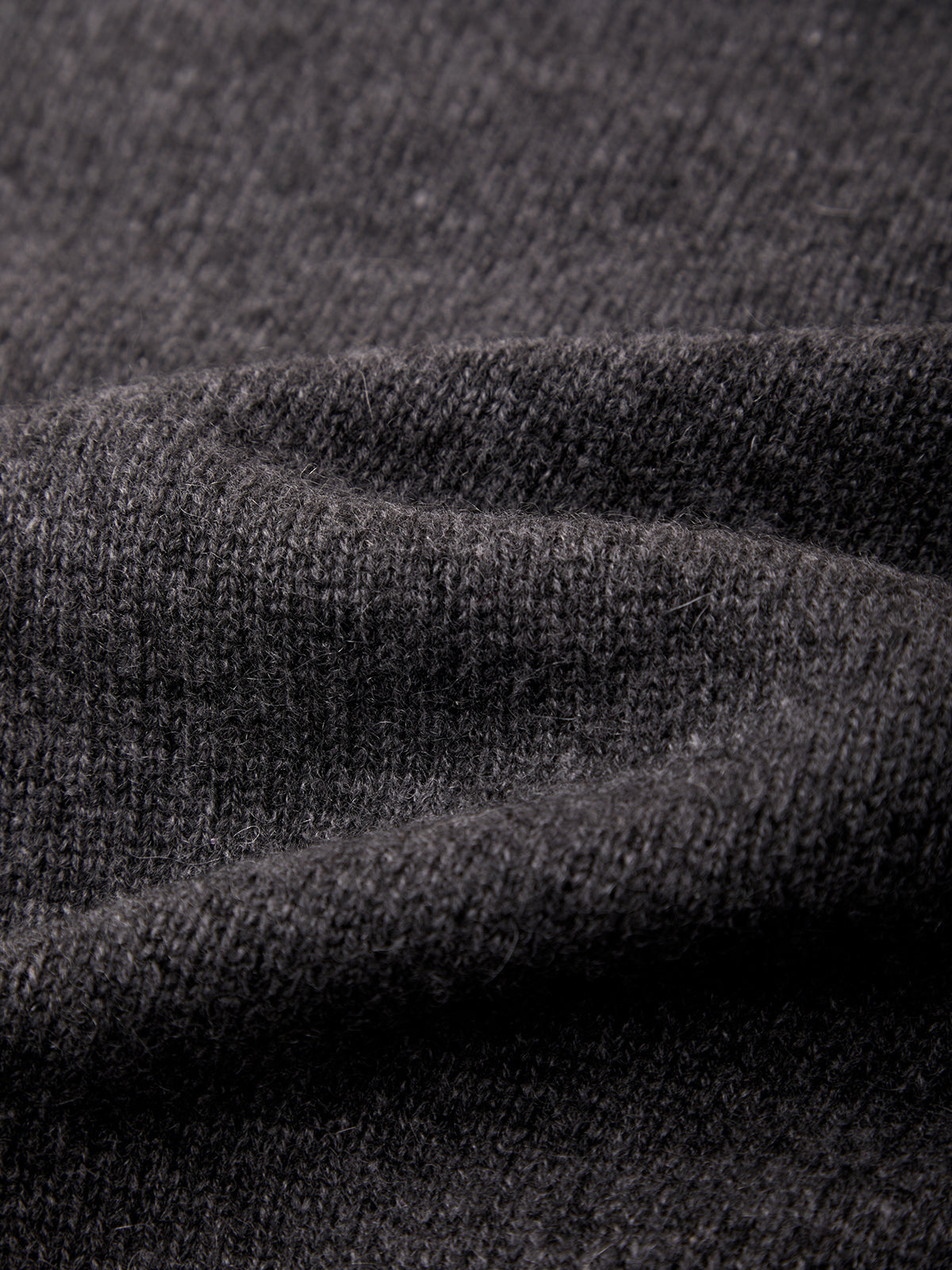 Close-up of dark charcoal gray knit fabric with soft folds showing the texture and weave.