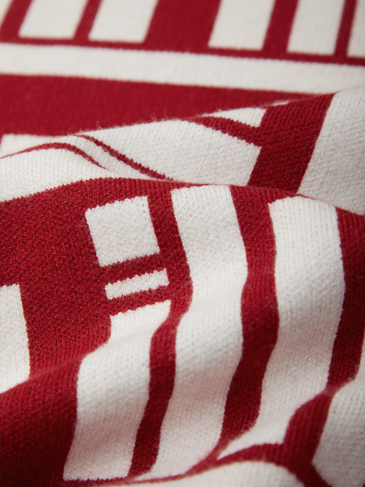 Close-up of a red and white striped knit fabric with a geometric pattern, showing the texture of the yarn.