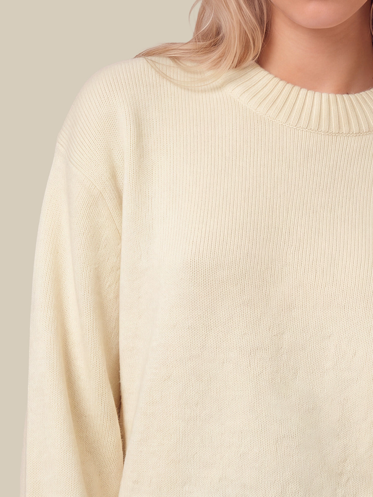 Close-up of a person wearing a white-colored ribbed knit sweater against a light beige background.