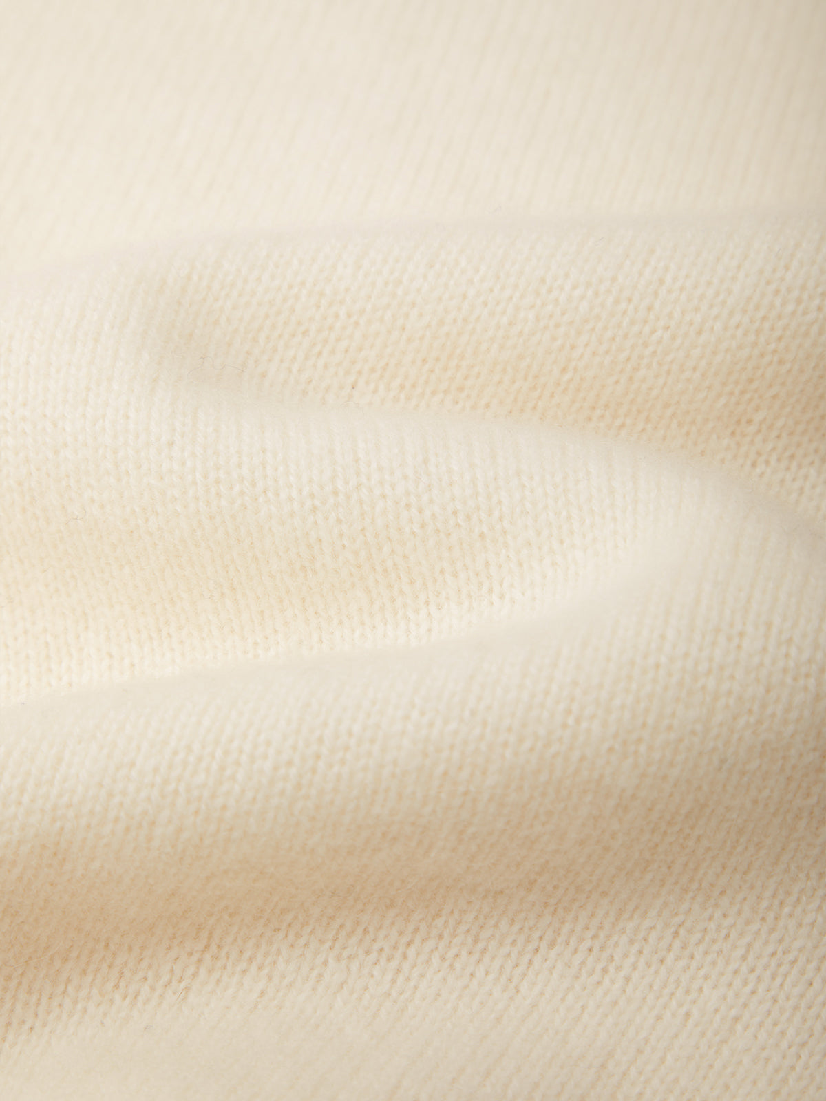 A close-up of soft white-colored knit fabric with a fine ribbed texture and gentle folds.