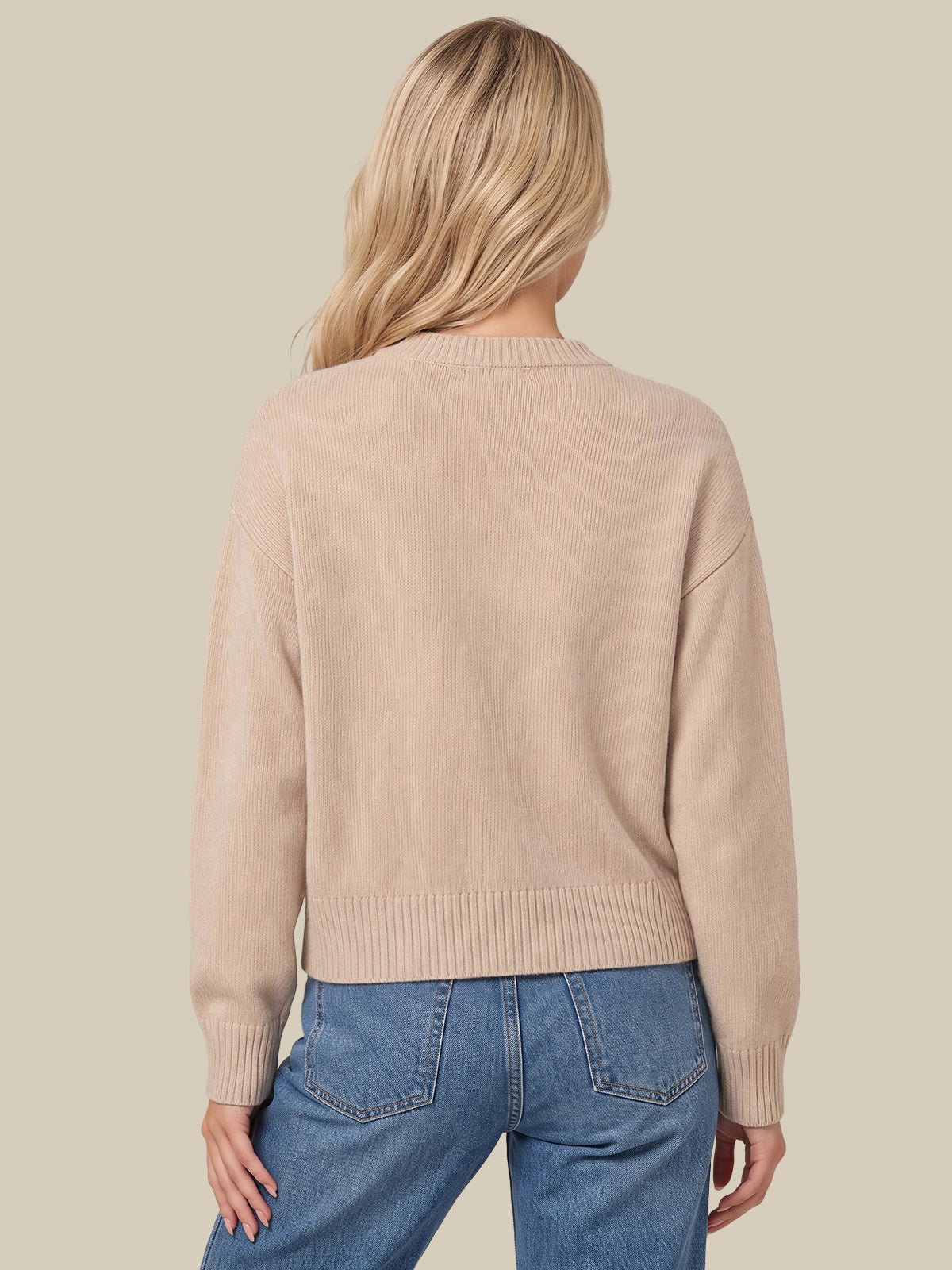 A woman shown from the back wearing a light beige knit sweater and blue jeans against a solid beige background.