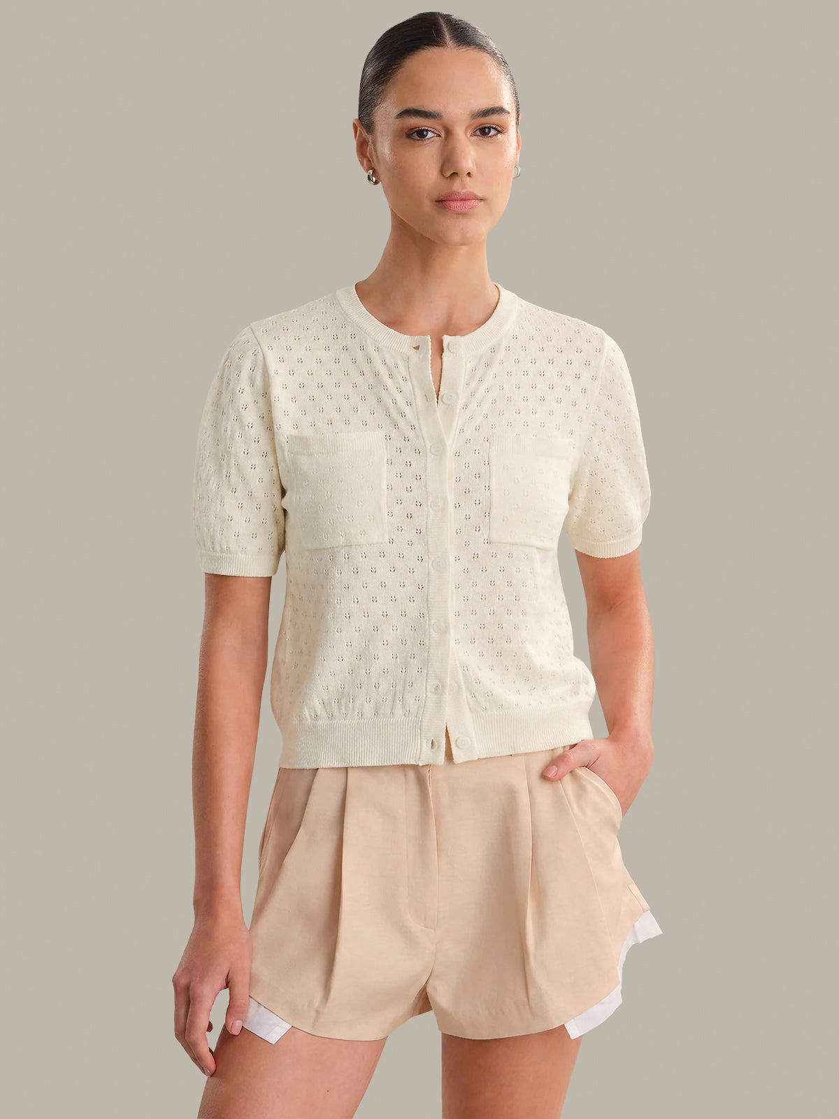 Woman wearing a cream-colored top and beige shorts against a gray background