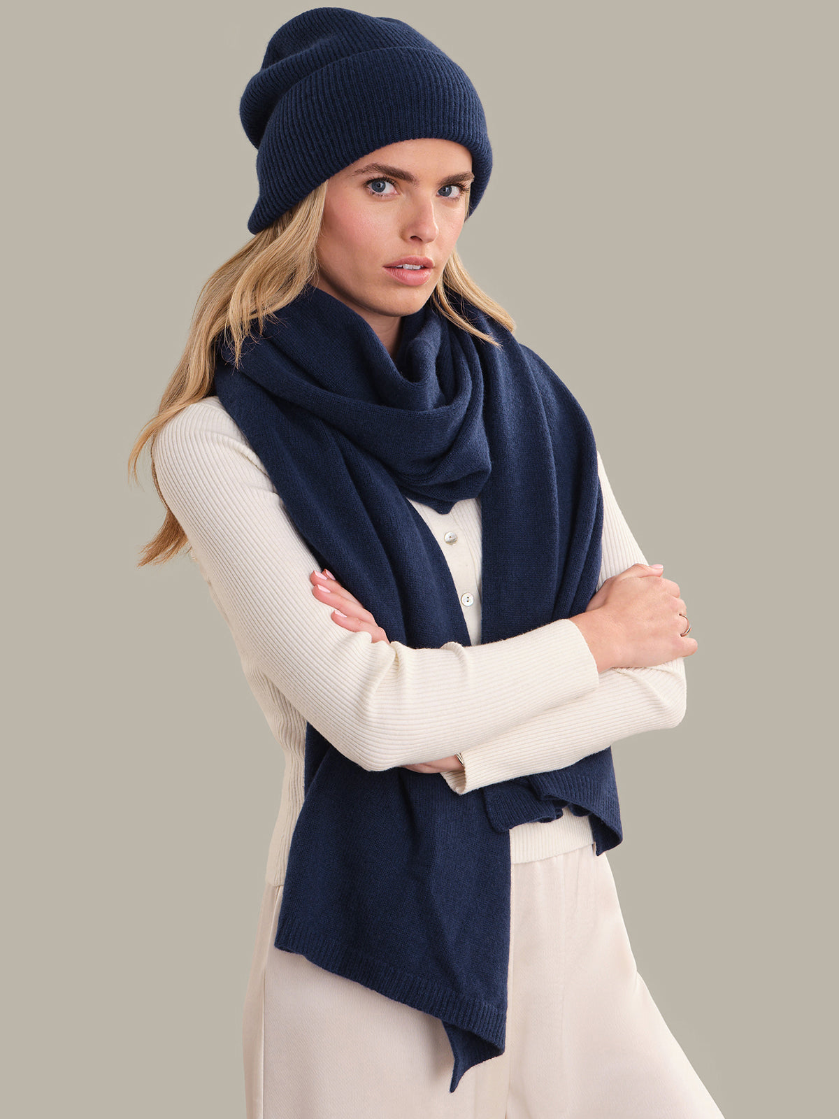 Woman wearing a navy blue beanie and scarf against a gray background