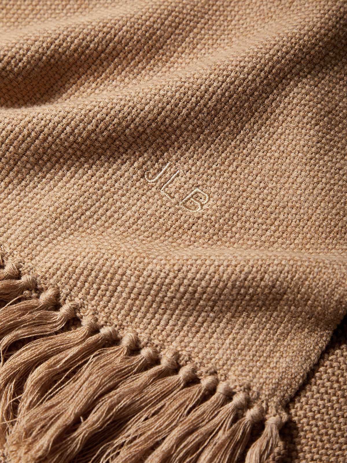 Close-up of a brown woven fabric with tassels and a brand logo.