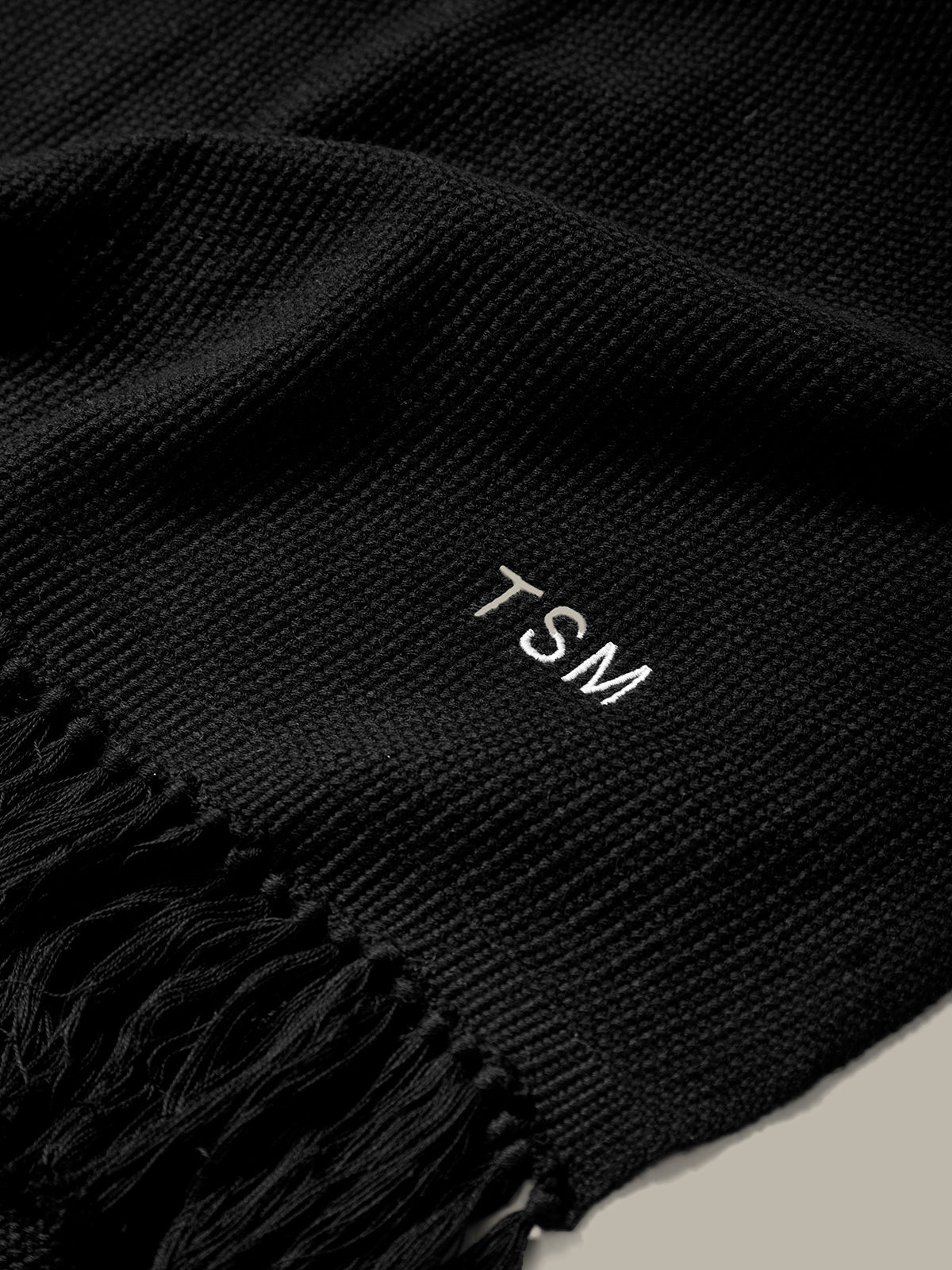 Black scarf with 'TSM' embroidery on a neutral background