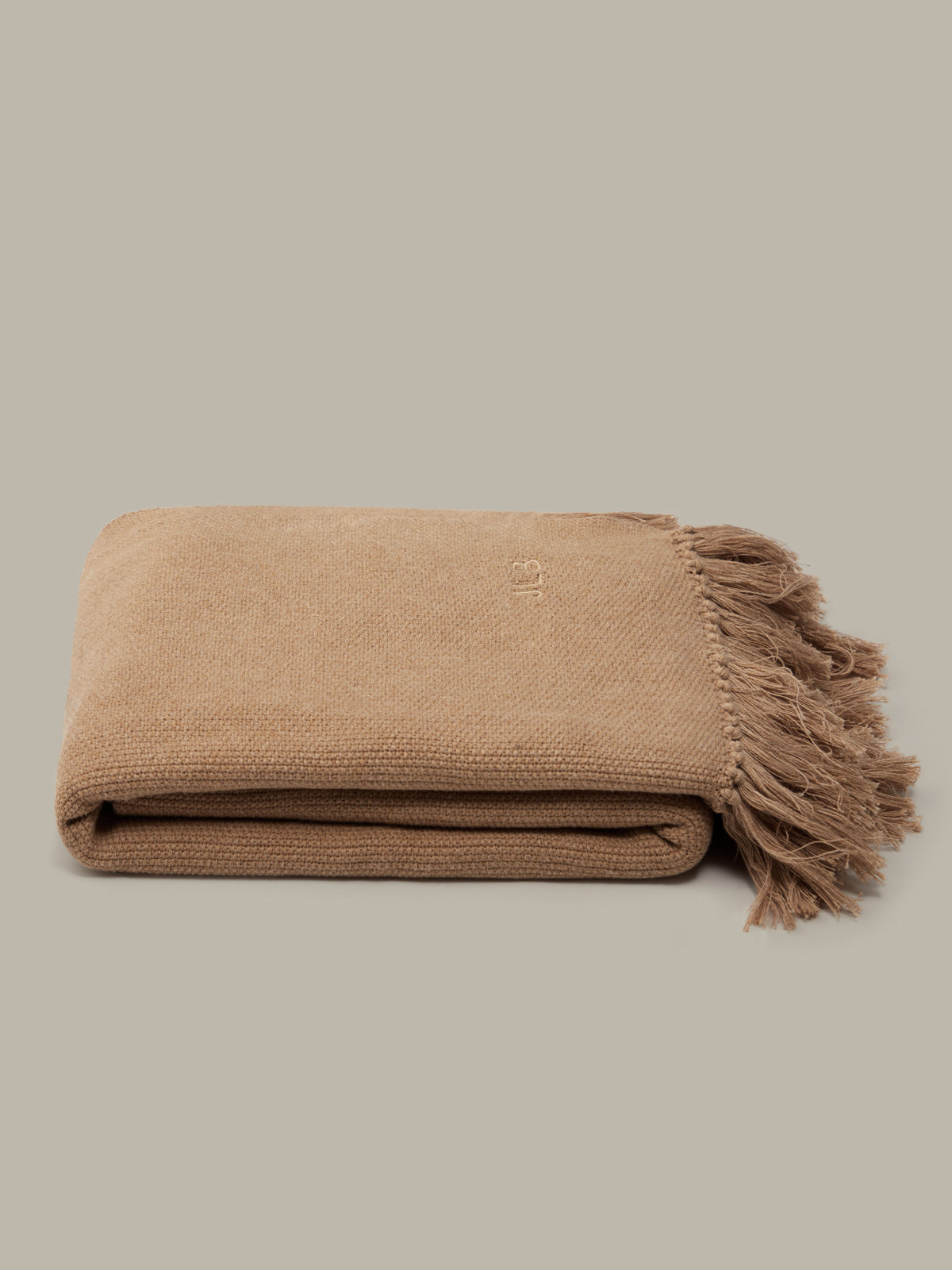 Folded beige blanket with frayed edges on a light beige background