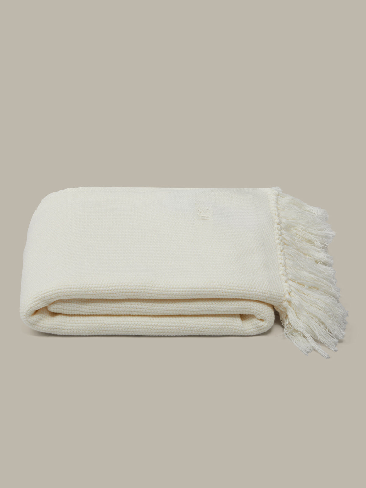 Folded beige blanket with tassels on a beige background