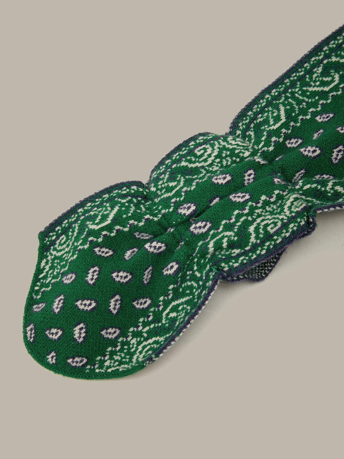 A green knitted bow tie with a white paisley pattern, shown on a solid beige background.