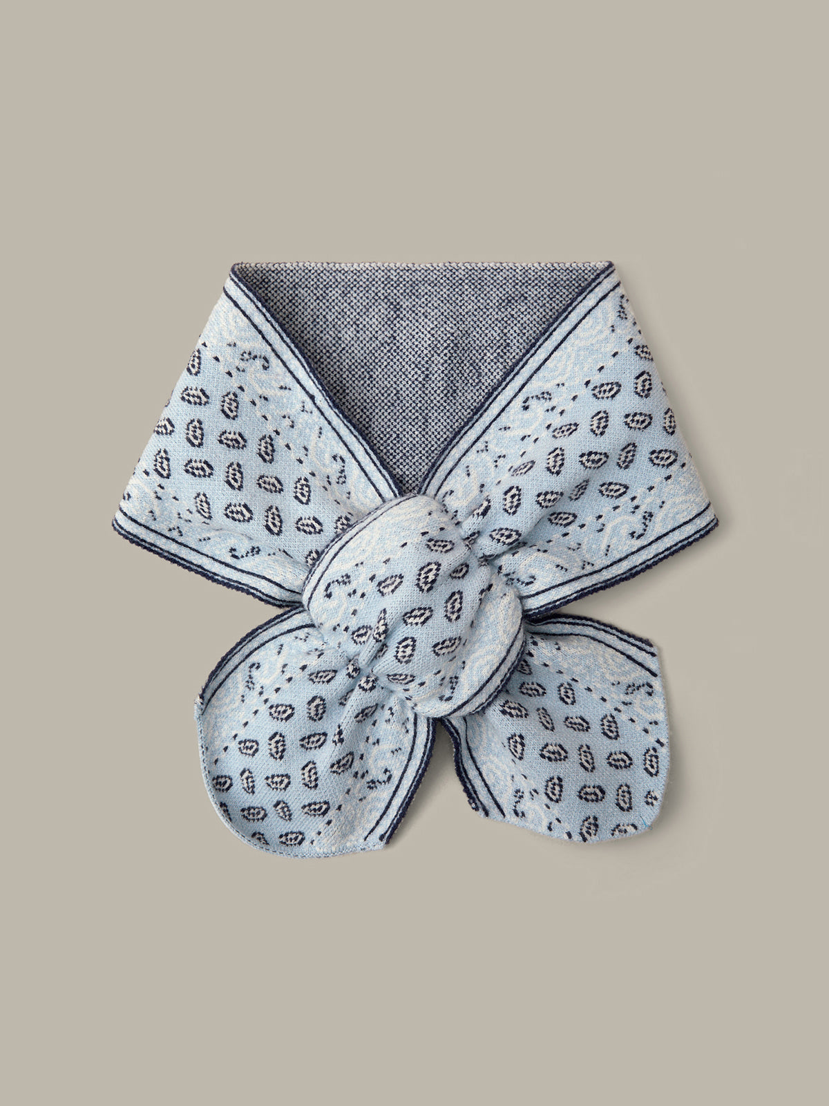 A folded light gray fabric accessory with a small black paisley pattern and a dark gray textured inner lining, displayed on a solid beige background.