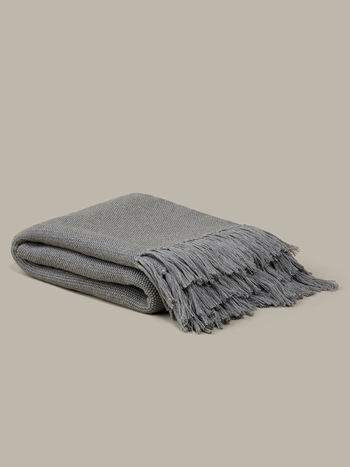 Folded gray blanket with fringes on a beige background