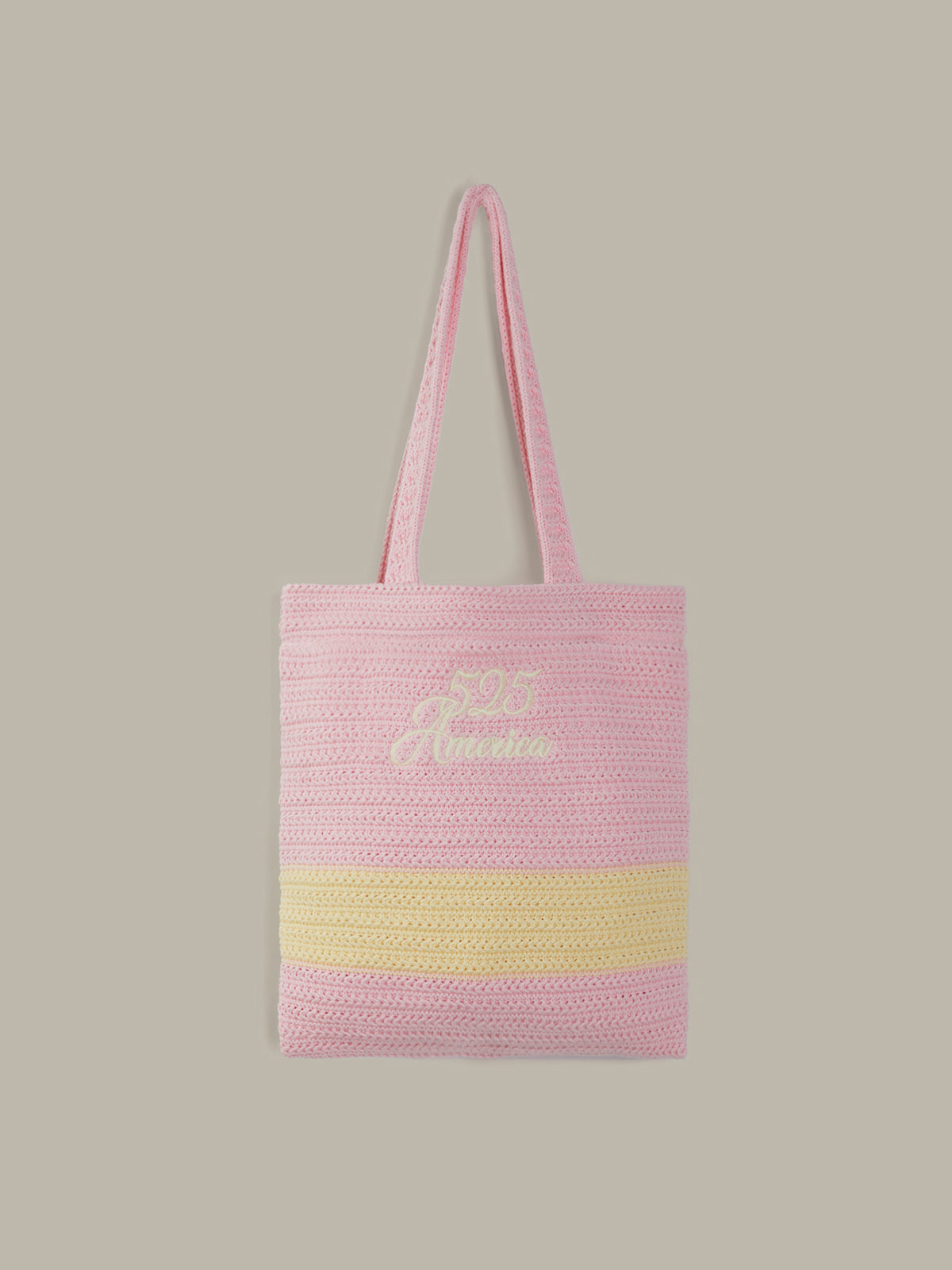 A pink woven tote bag with a horizontal yellow stripe near the bottom and a white embroidered logo on the front, shown against a solid taupe background.