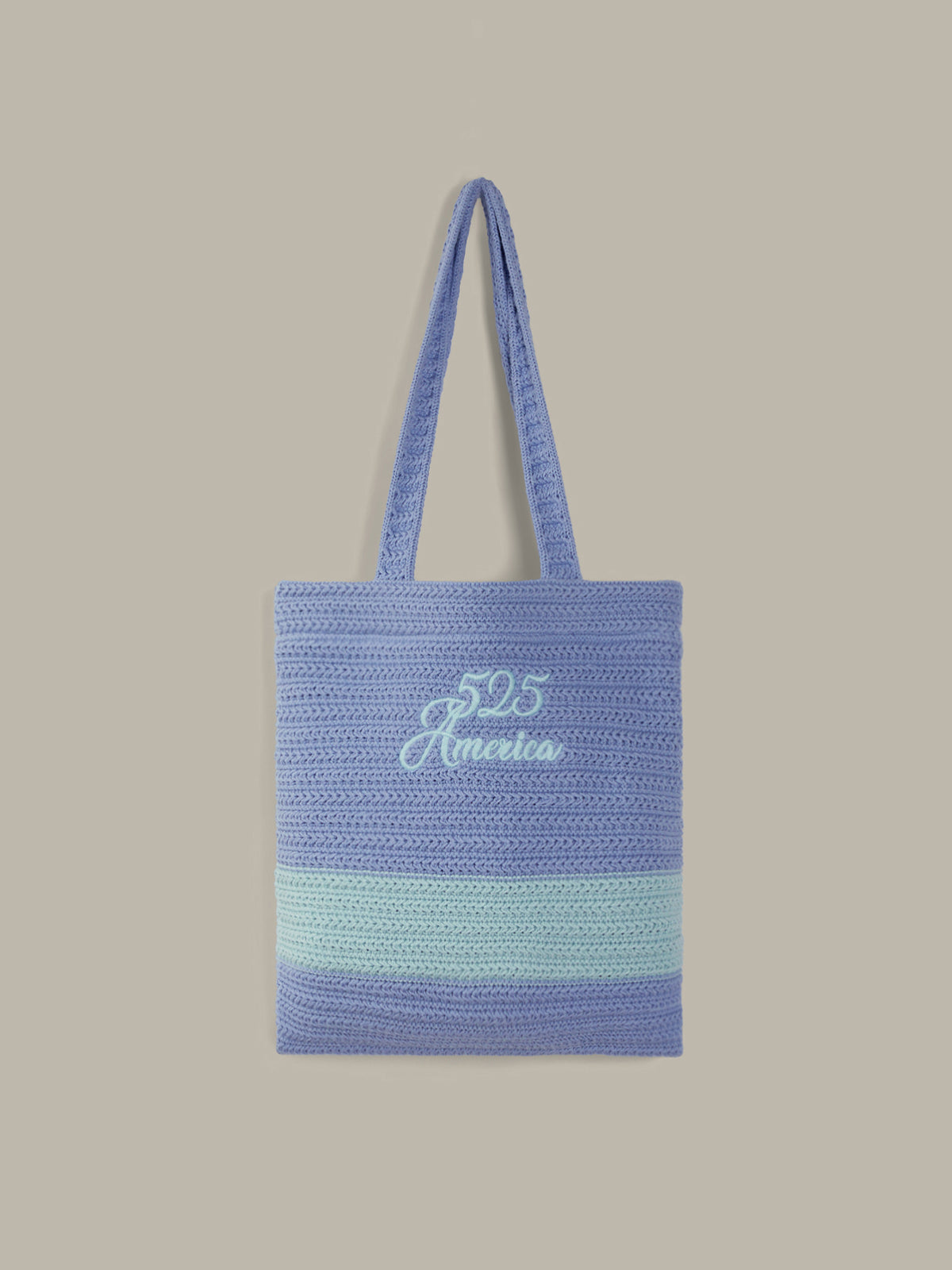 A woven tote bag in shades of blue and light green, featuring the text '525 America' embroidered in white on the front, set against a solid beige background.