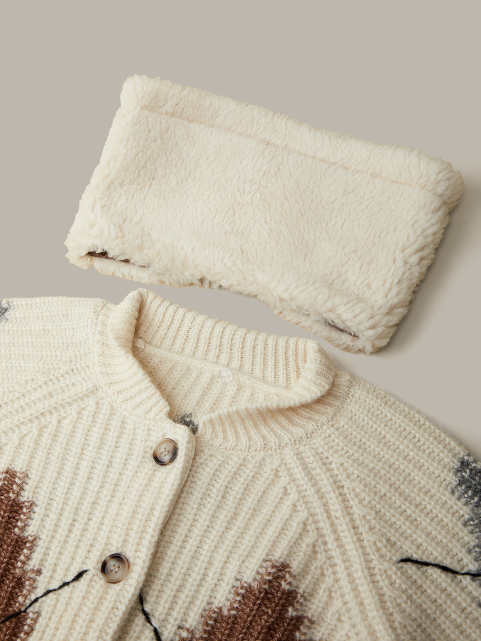 Knitted cardigan with pattern and folded fabric on a neutral background