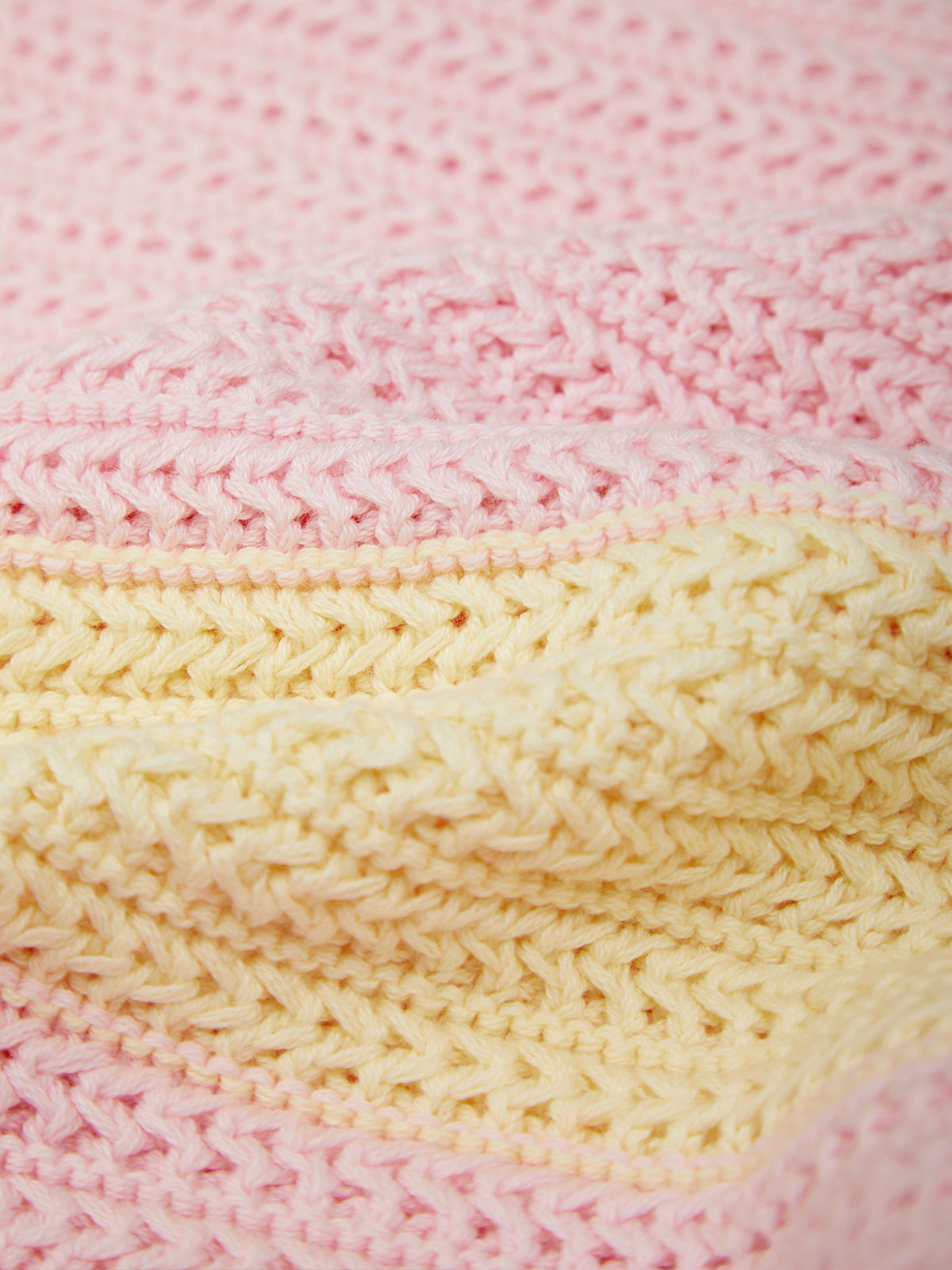Close-up of a knitted textile with alternating horizontal bands of soft pink and pale yellow yarn, showing the texture and stitch pattern in detail.