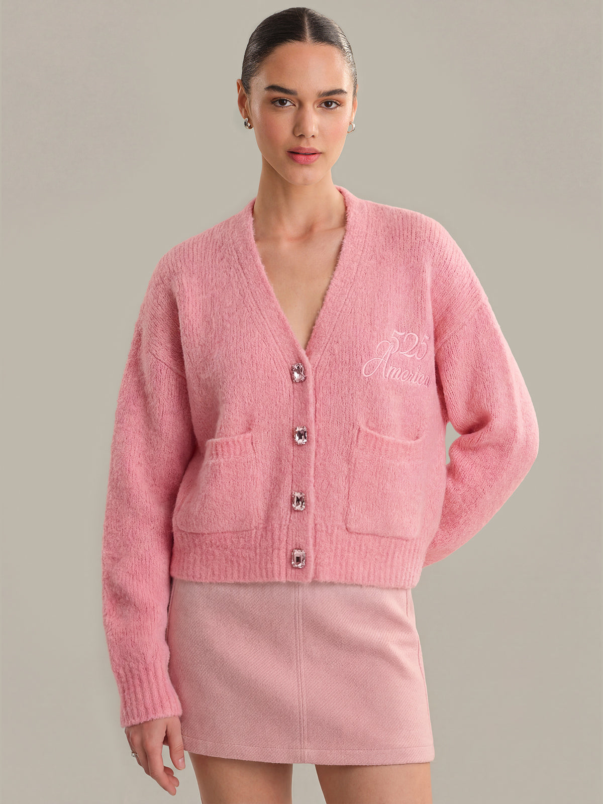 Woman wearing a pink cardigan with a brand logo on a gray background