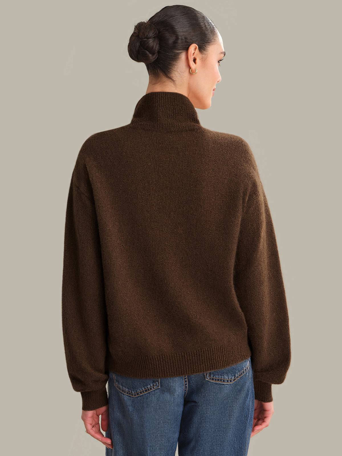Person wearing a brown sweater and blue jeans on a plain background
