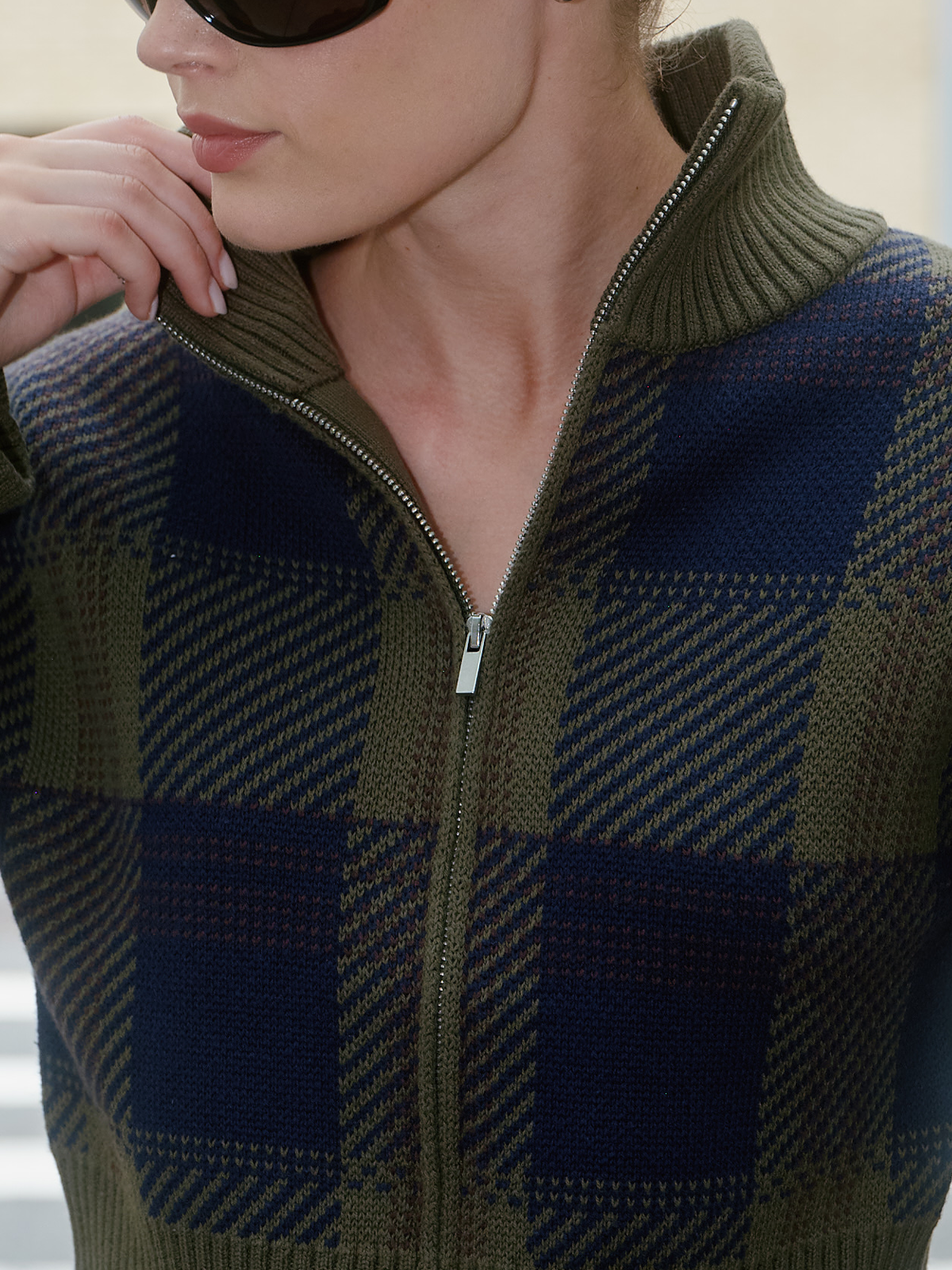 Close-up of a woman wearing a ribbed knit zip-front sweater with an olive green and navy blue plaid pattern.