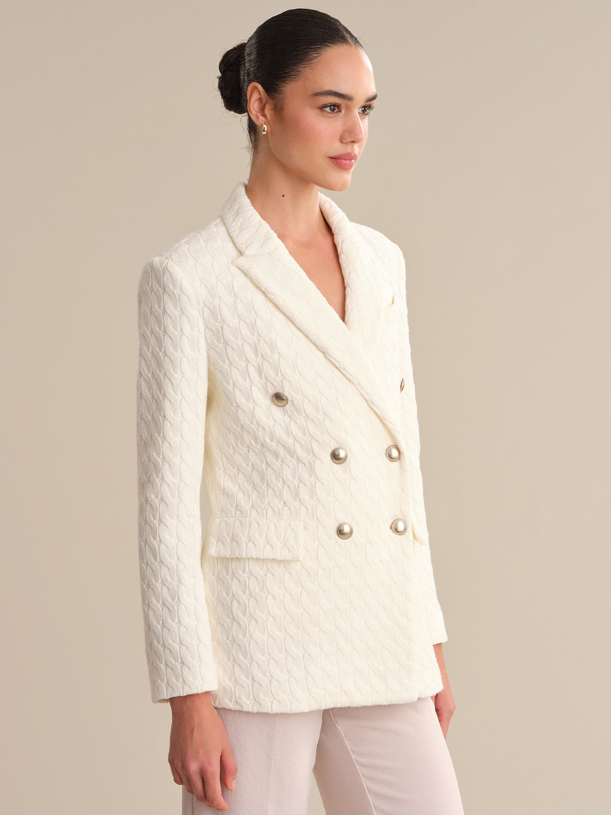 Woman wearing a white textured blazer with gold buttons on a beige background